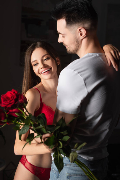 man in white t-shirt near happy woman in sexy underwear holding red roses - Foto, afbeelding