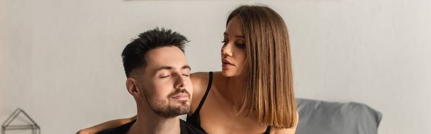 young and sensual woman looking at man with closed eyes in bedroom, banner - Foto, Bild