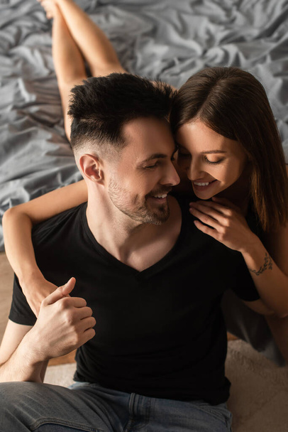 high angle view of happy young woman hugging smiling man in black t-shirt in bedroom - Foto, Imagem
