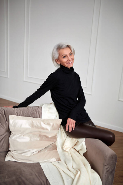 Stylish mature woman on sofa in living room - Valokuva, kuva