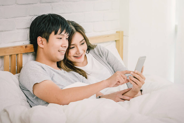 Closeup Happy Asian Lover or couple using technology smart phone on the bed in bed room at modern home, boyfriend pointing to the mobile phone, Lover and life style concept, - Φωτογραφία, εικόνα