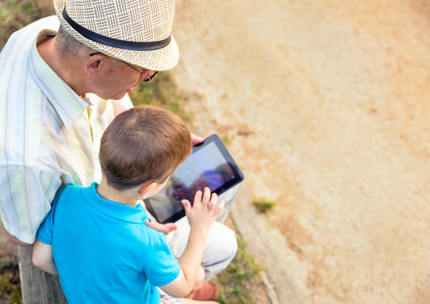 Внук и дедушка с помощью планшета на улице
 - Фото, изображение