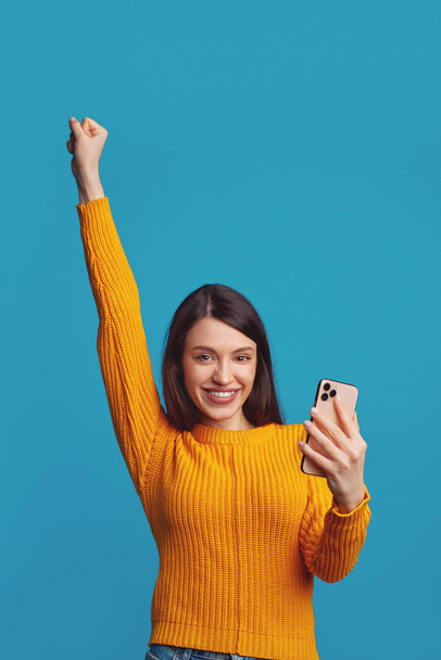 Girl raises clenched fist with triumph, celebrate victory, holds modern cell phone - Foto, Imagem