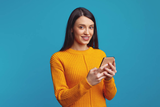 Smiling young woman holds modern cellular, sends message in social networks - Fotografie, Obrázek