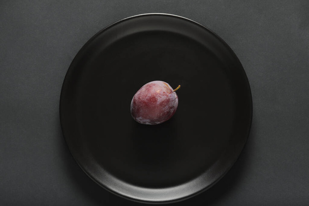 ciruelas frescas en un plato negro - Foto, Imagen