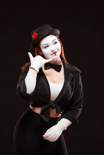 Portrait of female mime artist performing, isolated on black background. Woman is pretending speaking by the phone - Фото, зображення