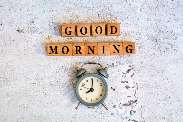 Texto de la buena mañana sobre cubos de madera y reloj despertador sobre fondo de textura gris - Foto, imagen