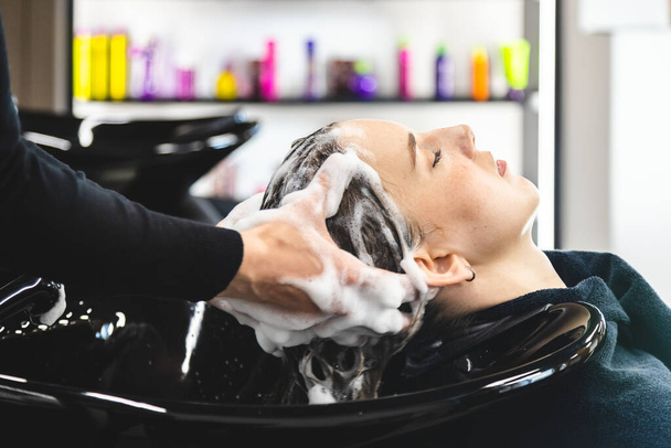 Master woman hairdresser gently washes the girls hair with shampoo and conditioner before styling in a beauty salon. - Photo, Image