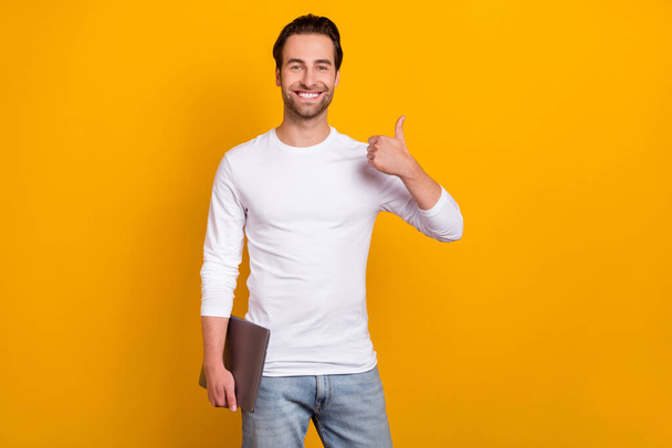 Photo of nice brunet millennial guy hold laptop show thumb up wear white outfit isolated on bright yellow color background - Fotografie, Obrázek