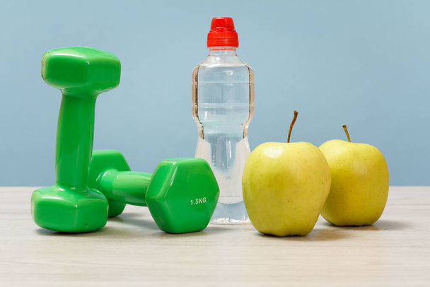 Spor için dambıllar, elmalar ve mavi arka planda bir şişe su.. - Fotoğraf, Görsel