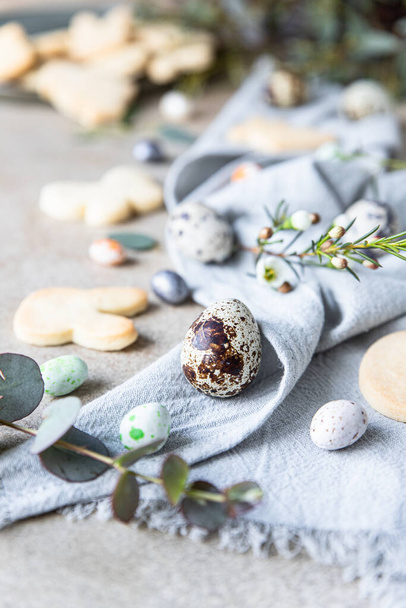 Easter cookies with candies shaped eggs, floral decor and quail eggs on linen napkin, stone background. Holiday concept. - Foto, Imagen