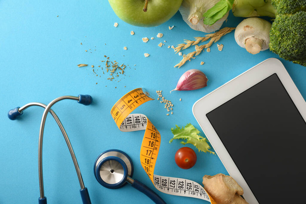 Digitális tabletta mérőszalaggal és sztetoszkóppal a kék asztalon zöldségekkel. Első látásra. Horizontális összetétel. - Fotó, kép