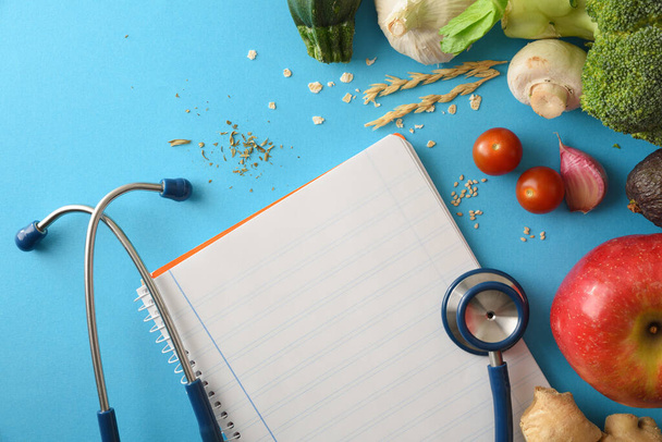 Health care guidelines with natural balanced food with fruits and vegetables and notepad with blank sheet on blue table. Top view. Horizontal composition. - Fotó, kép