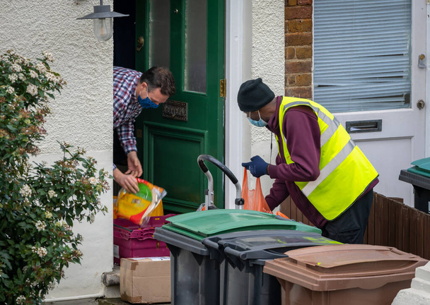 London.UK-02.06.2021: a Sainsbury's supermarket delivery man making an online grocery delivery to a customer's door front observing Covid-19 safety rules with face covering and social distancing. - Фото, зображення