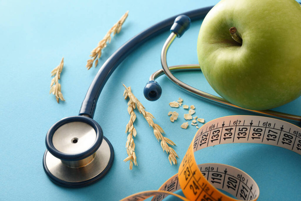 Nutritional medical health background with stethoscope tape measure with apple and ears of oatmeal on blue background. Elevated view. - Foto, immagini
