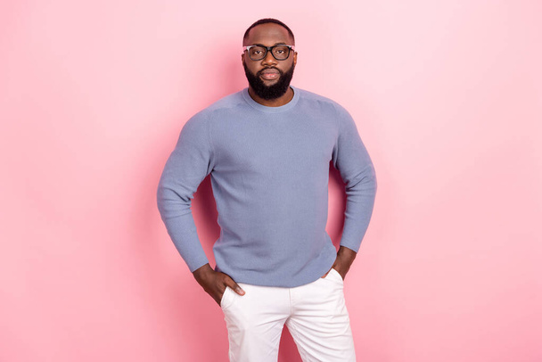 Photo of serious confident african guy dressed grey sweater spectacles hands pockets isolated pink color background - Fotó, kép
