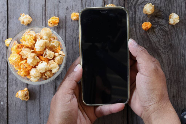 karmelowa przekąska z popcornem i smartfon pod ręką - Zdjęcie, obraz