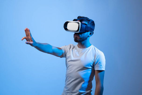 Fiatal szakállas férfi VR szemüveg választás lehetőségek, miközben virtuális valóság tapasztalat egy sötét szobában. - Fotó, kép