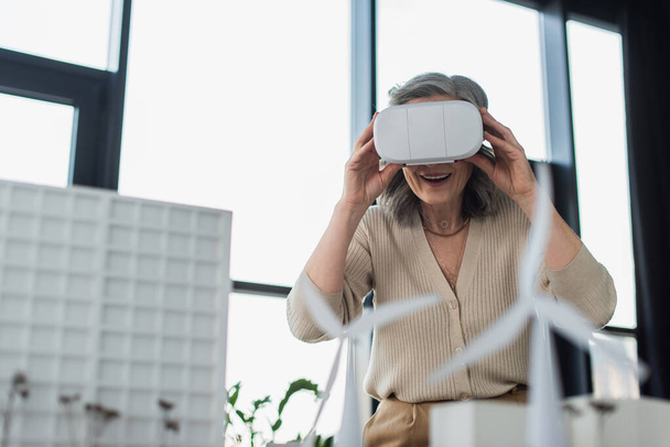 Mature businesswoman in vr headset near models of buildings in office  - Foto, immagini