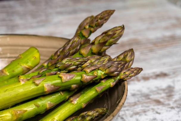 Raw asparagus in bowl on wooden desk - Фото, зображення