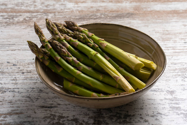 Raw asparagus in bowl on wooden desk - Фото, изображение
