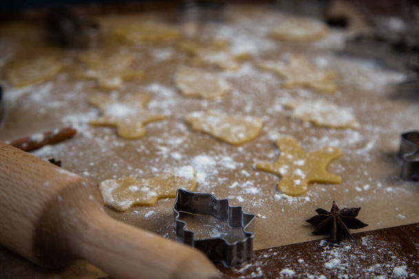 There are ready-made cookies of different shapes on the parchment, a rolling pin, cookie cutters and a sieve with flour are lying nearby, flour is scattered everywhere - Foto, immagini
