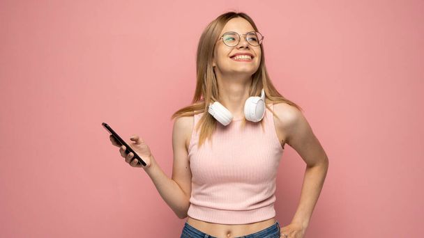 Young blonde woman in a glasses and pink t-shirt over isolated pink background sending a message with the mobile. - Zdjęcie, obraz