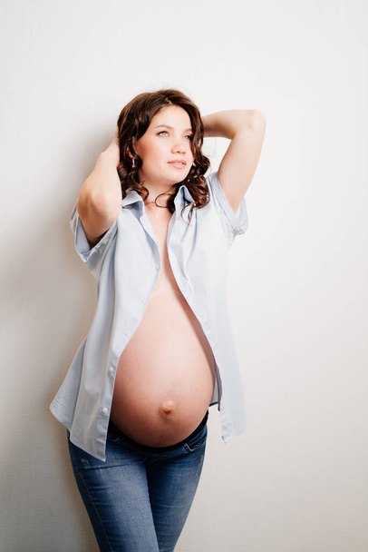 attractive pregnant woman in jeans and a shirt on a naked body. womens health - Foto, immagini