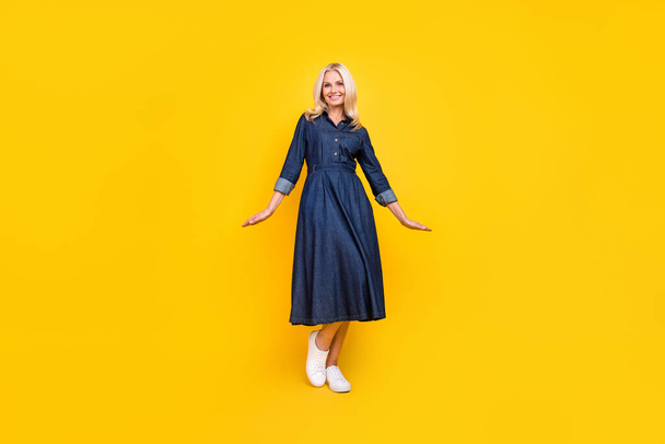 Фото красивої солодка леді пенсіонерка одягнена в джинсове вбрання, усміхнений ходьба ізольований жовтий кольоровий фон
 - Фото, зображення