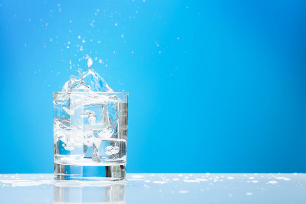 Buz küplü su bardağı ve fotokopi alanı ile mavi arkaplan üzerine sıçrıyor - Fotoğraf, Görsel