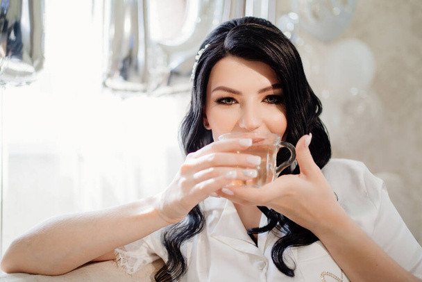 happy brunette bride drinks tea the morning before the wedding.  - Фото, изображение