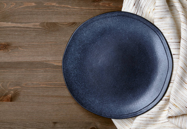 Dark ceramic plate on a crumpled linen tablecloth on a dark wooden table - Foto, Imagem
