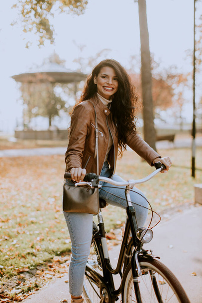 Pretty young woman riding bicycle on autumn day - Photo, Image