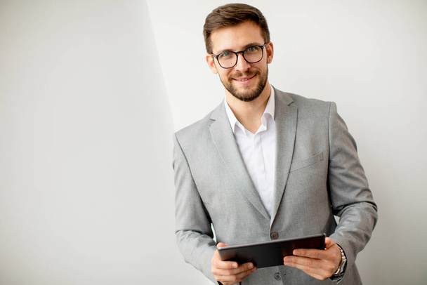 Handsome young modern businessman using digital tablet by the wall in the office - Fotoğraf, Görsel