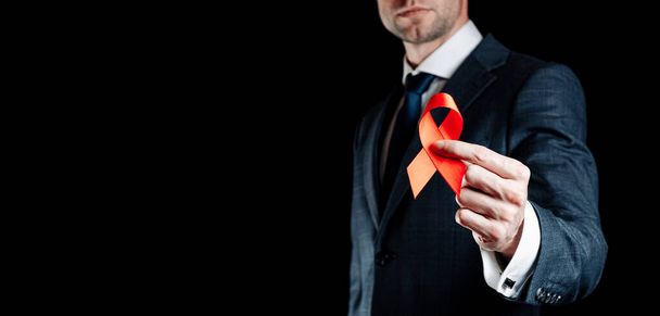 Hiv day. Red ribbon in hiv world day isolated on black background. Man holding awareness aids and cancer symbol. Aging Health month concept - Zdjęcie, obraz