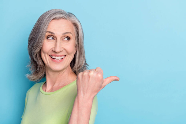 Photo of charming happy nice old woman look point finger empty space choose isolated on blue color background - Foto, immagini