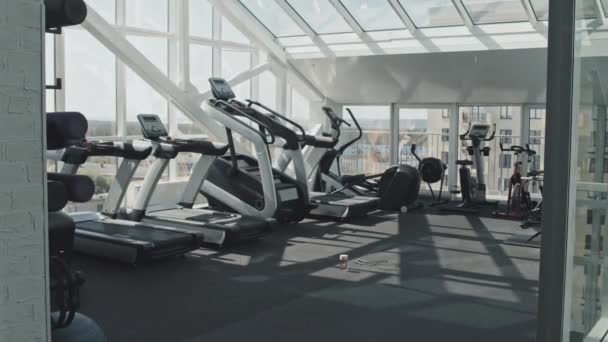 Intérieur d'une salle de gym moderne avec appareils de fitness et murs en verre et plafond - Séquence, vidéo