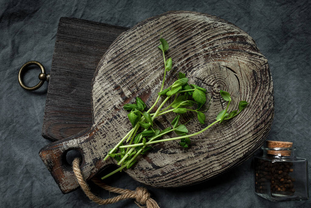A bunch of cut micro-greenery on an old wooden boards and a bottle of spices for a culinary theme design. Diagonal arrangement. Copy space - Zdjęcie, obraz