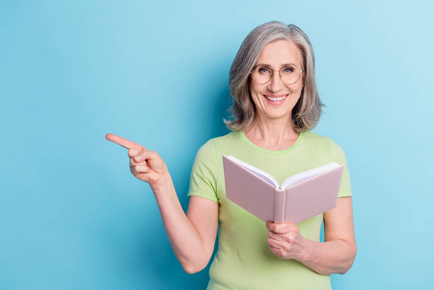 Photo of attractive old charming woman point finger empty space hold book isolated on pastel blue color background - Foto, immagini