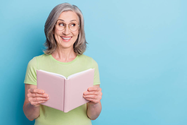 Photo of charming dreamy happy old woman hold book novel look empty space isolated on blue color background - Foto, immagini
