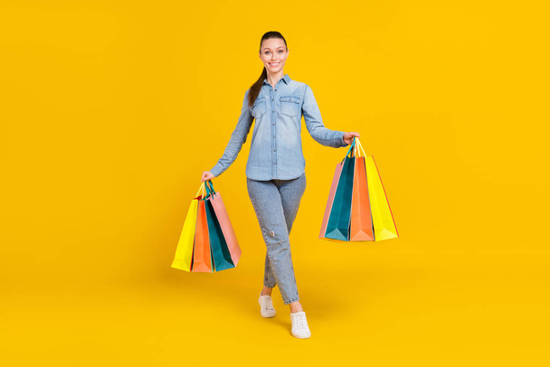 Full body photo of cheerful lovely young woman hold hands bags shopping smile isolated on yellow color background - Фото, изображение