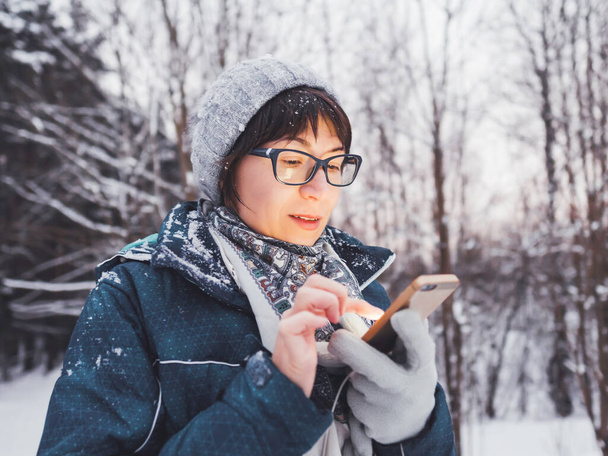 Woman with smartphone in winter forest. Using electronic gadget for navigation, taking photos, communication of pocket light. - Photo, Image