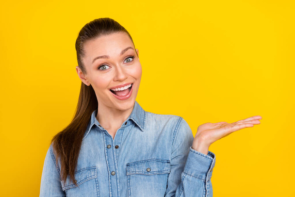 Photo of excited shiny young lady dressed jeans shirt open mouth holding arm empty space smiling isolated yellow color background - Foto, Bild
