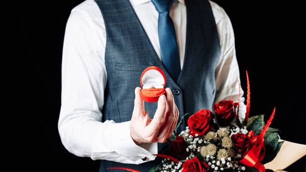 Cásate conmigo. Joven hombre feliz sosteniendo caja de regalo roja con anillo de compromiso de diamantes, ramo de rosas rojas. Anillo de matrimonio de compromiso - Foto, imagen