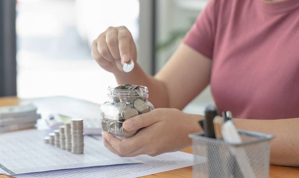 Woman puts a coin dollar in a jar, Saving money for future growth and knowing how to manage your spending wisely, Saving money for business growth or long-term profitability. - Photo, Image