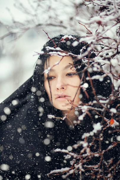 νεαρή μελαχρινή γυναίκα ποζάρουν με χιονισμένα κλαδιά θάμνων - Φωτογραφία, εικόνα
