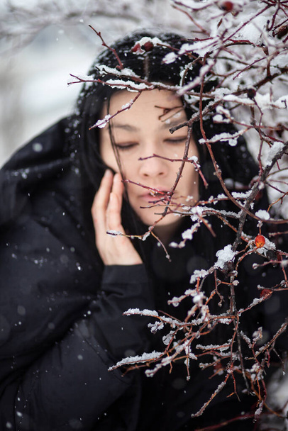 νεαρή γυναίκα αγγίζοντας το πρόσωπο με το χέρι δει μέσα από χιονισμένα κλαδιά θάμνος - Φωτογραφία, εικόνα