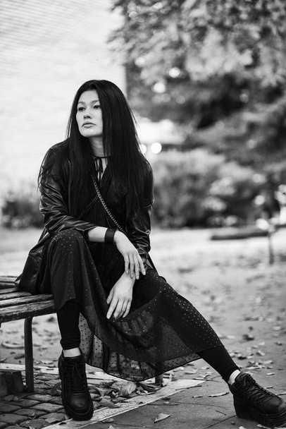 preto e branco tiro de jovem mulher sentado no banco no parque com folhas caídas - Foto, Imagem