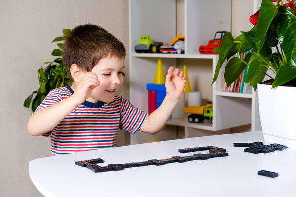 Un garçon heureux de 4 ans joue à un jeu de société de dominos, s'amuse et aime le jeu - Photo, image