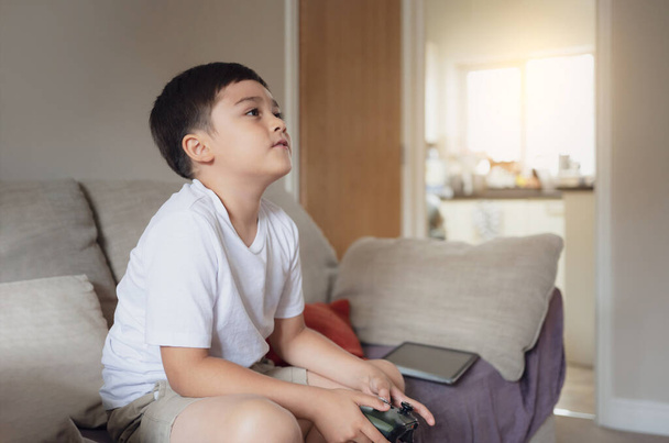 Portrait of happy kid holding a video game control. Child playing a online game at home,Young boy siting on a sofa having fun playing with a toy and relaxing on the weekend, New lifestyle after covid - Foto, Bild